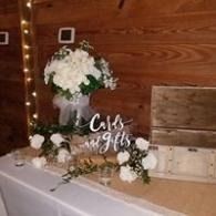 Table display with white flowers, greenery, wooden crates, and a “Cards” sign against a wood-paneled wall