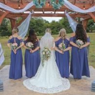Wedding party under decorated pergola: bride in white with bouquet, bridesmaids in blue dresses