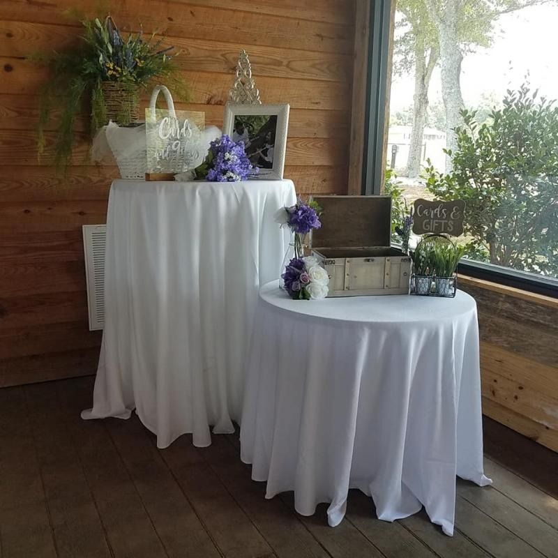 Two white-draped tables with purple flowers and lanterns in a wooden porch setting