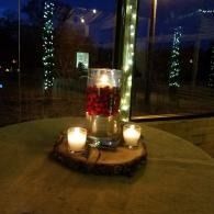 Candlelit centerpiece with red flowers in a glass vase on a table by a window at night