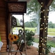 Decorated porch with sunflowers, large “S &” sign, and string lights overlooking a grassy yard