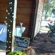 Welcome sign for friends on a porch with string lights and a wooden wall