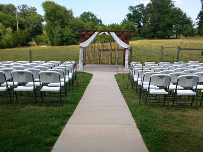Outdoor wedding aisle with white chairs and a floral arch in a grassy field