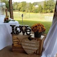Rustic wedding decor with “Love” sign, heart plaque, and flowers on a table overlooking a green field