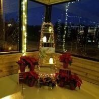 Festive holiday display with red poinsettias and a lit tower in a windowed room at dusk