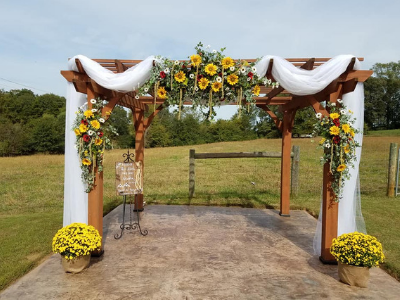 Decorated outdoor wedding arch with white drapes, sunflowers, and yellow flowers on a concrete patio
