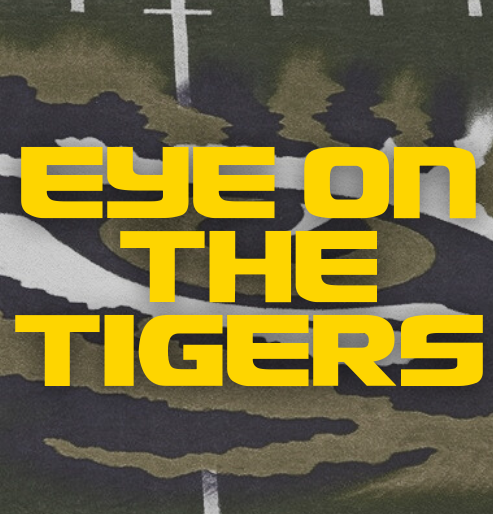 Yellow text reading “EYE ON THE TIGERS” over a dark camouflage background with a cross
