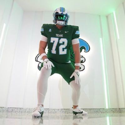 Green-uniformed football player in a helmet posing in a bright hallway with a Jaguars logo backdrop