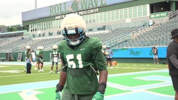 Football player in green uniform and helmet stands on a field in a stadium.