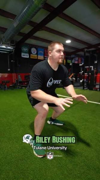 Athlete in black shirt and shorts crouches on indoor turf in a training facility.
