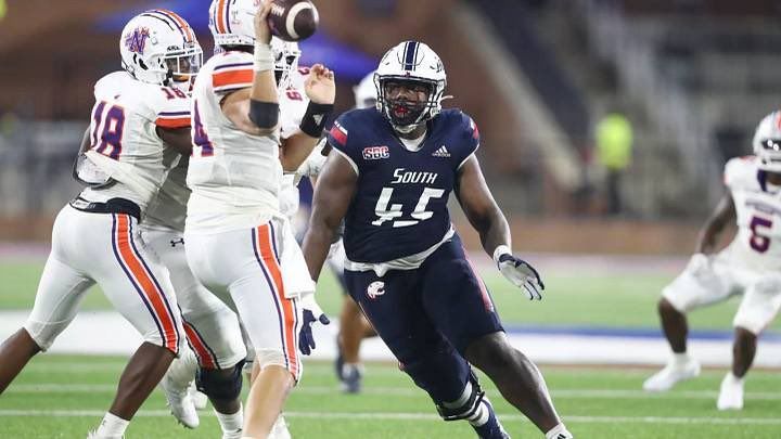 College football player in navy jersey runs with the ball while defenders in white close in on the field.