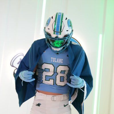 Tulane football player in blue jersey and white helmet adjusting gloves indoors
