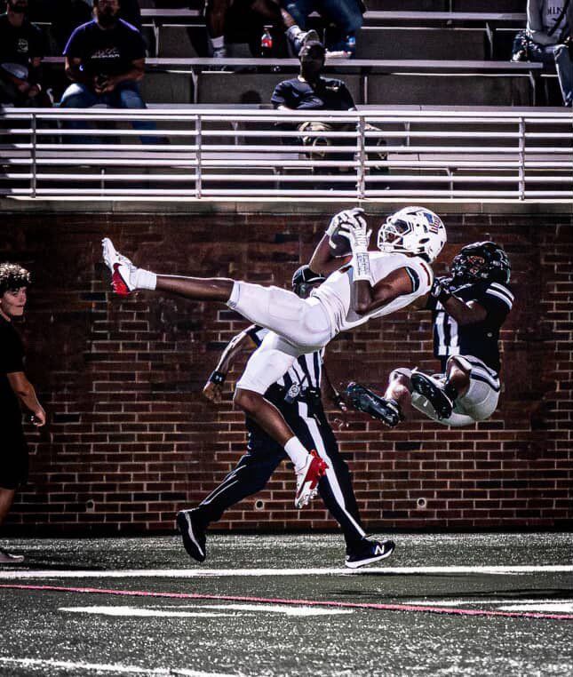 Two football players collide midair near the end zone in a night game.