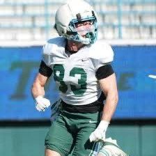 Football player in white and green uniform on the field, wearing a helmet and gloves.