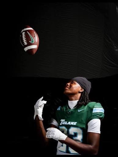 Tulane football player in green jersey and white gloves tracks a football against a dark background