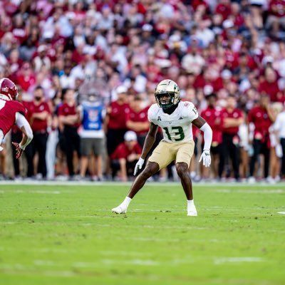 Football player in white jersey and gold pants ready on a green field, crowd blurred in the background