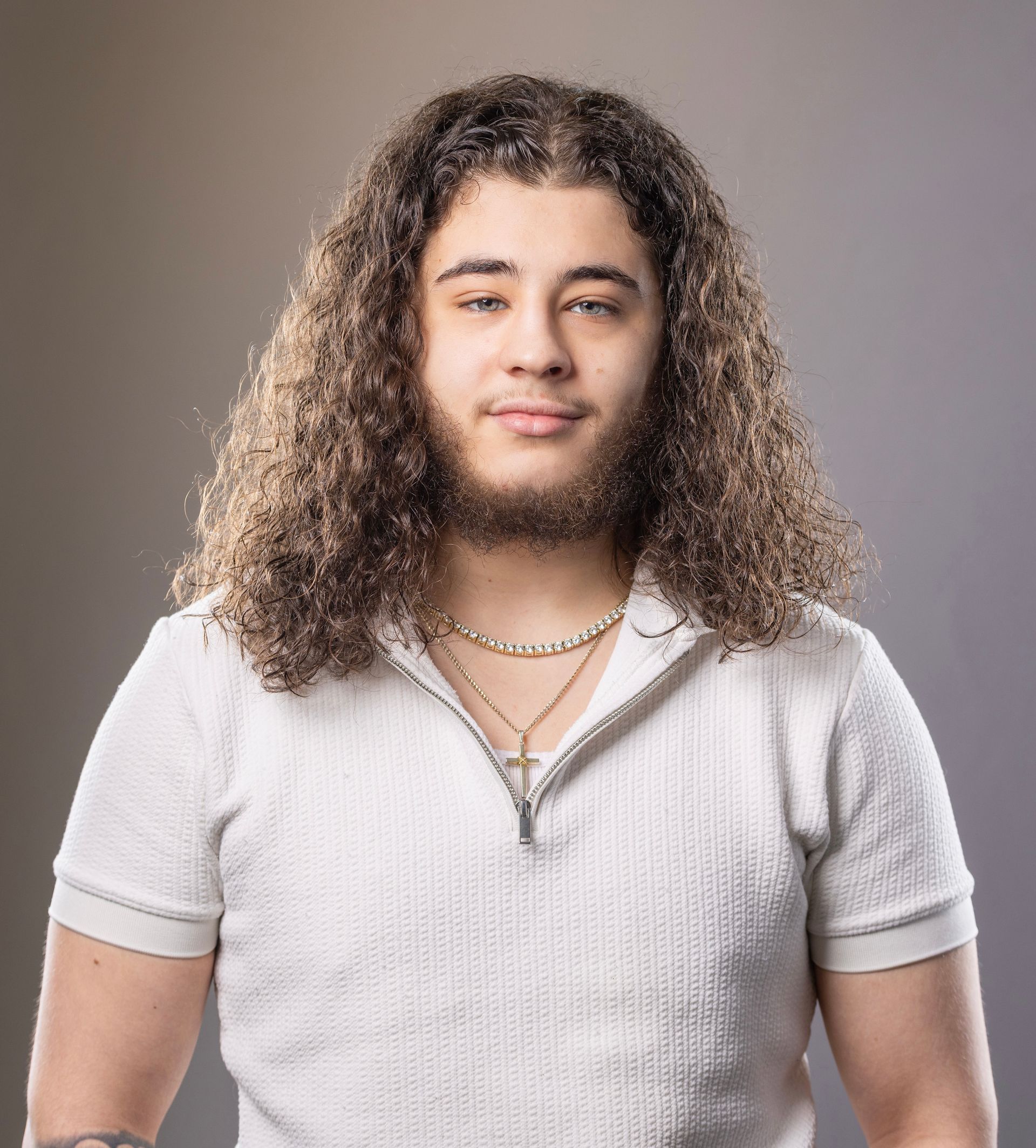 Person with curly hair in a white shirt, facing forward against a gray background.