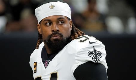 A man wearing a headband and a football jersey is sitting on the sidelines.