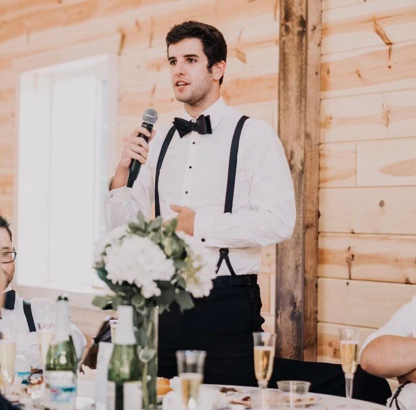A man in a tuxedo is speaking into a microphone