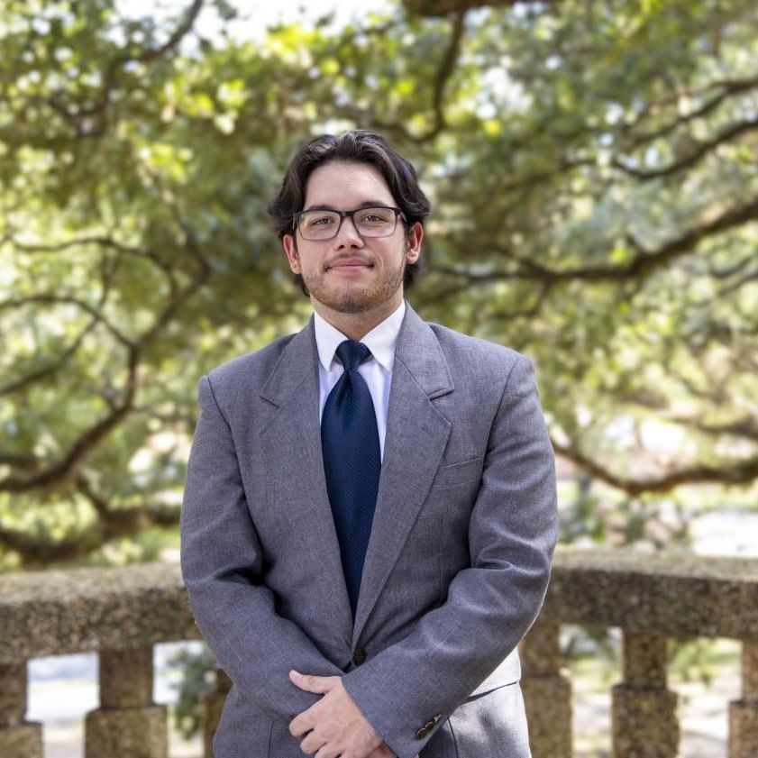 A man in a suit and tie is standing in front of a tree.