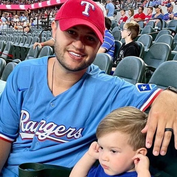A man wearing a rangers jersey is holding a baby