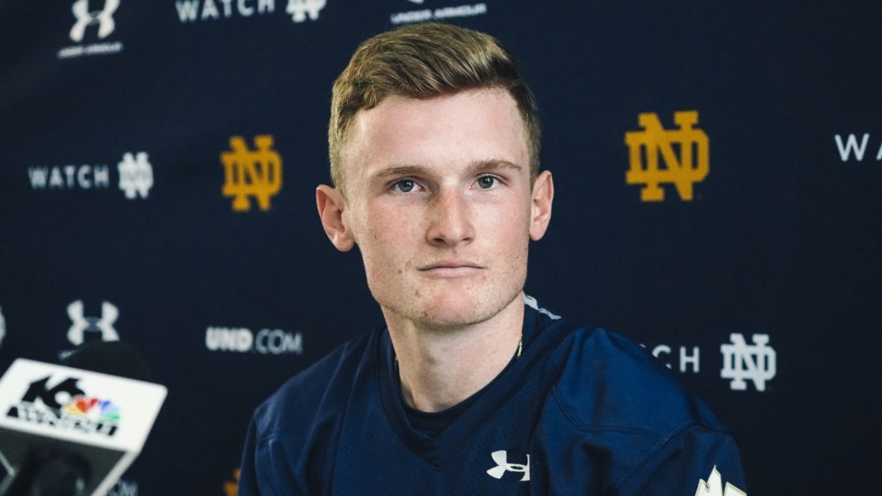 A young man in a blue shirt is sitting in front of a blue wall.