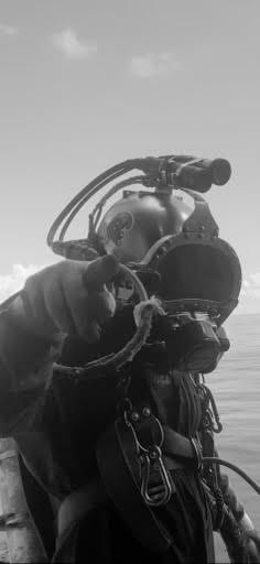 Scuba diver in gear holding camera underwater against a bright surface background