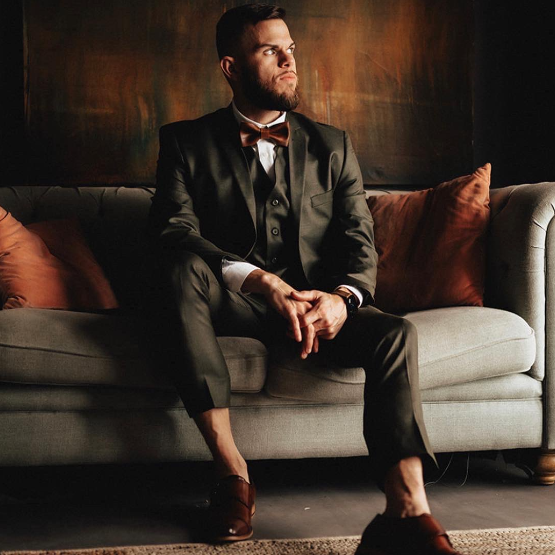 A man in a suit and bow tie is sitting on a couch.