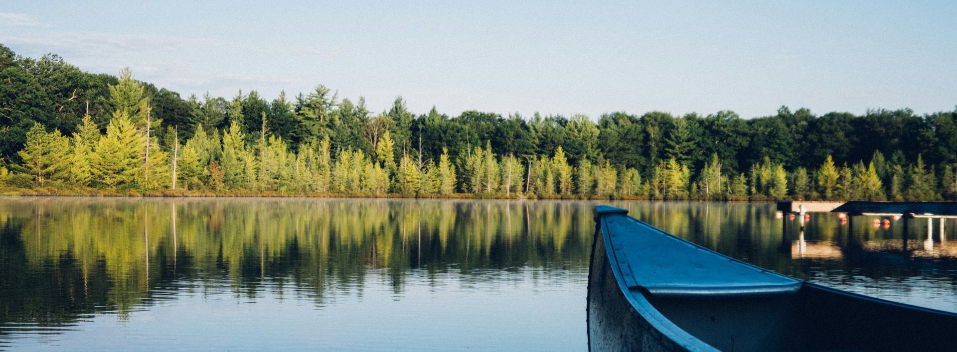 Photograph of a canoe on a peaceful lake with green trees and a clear blue sky
