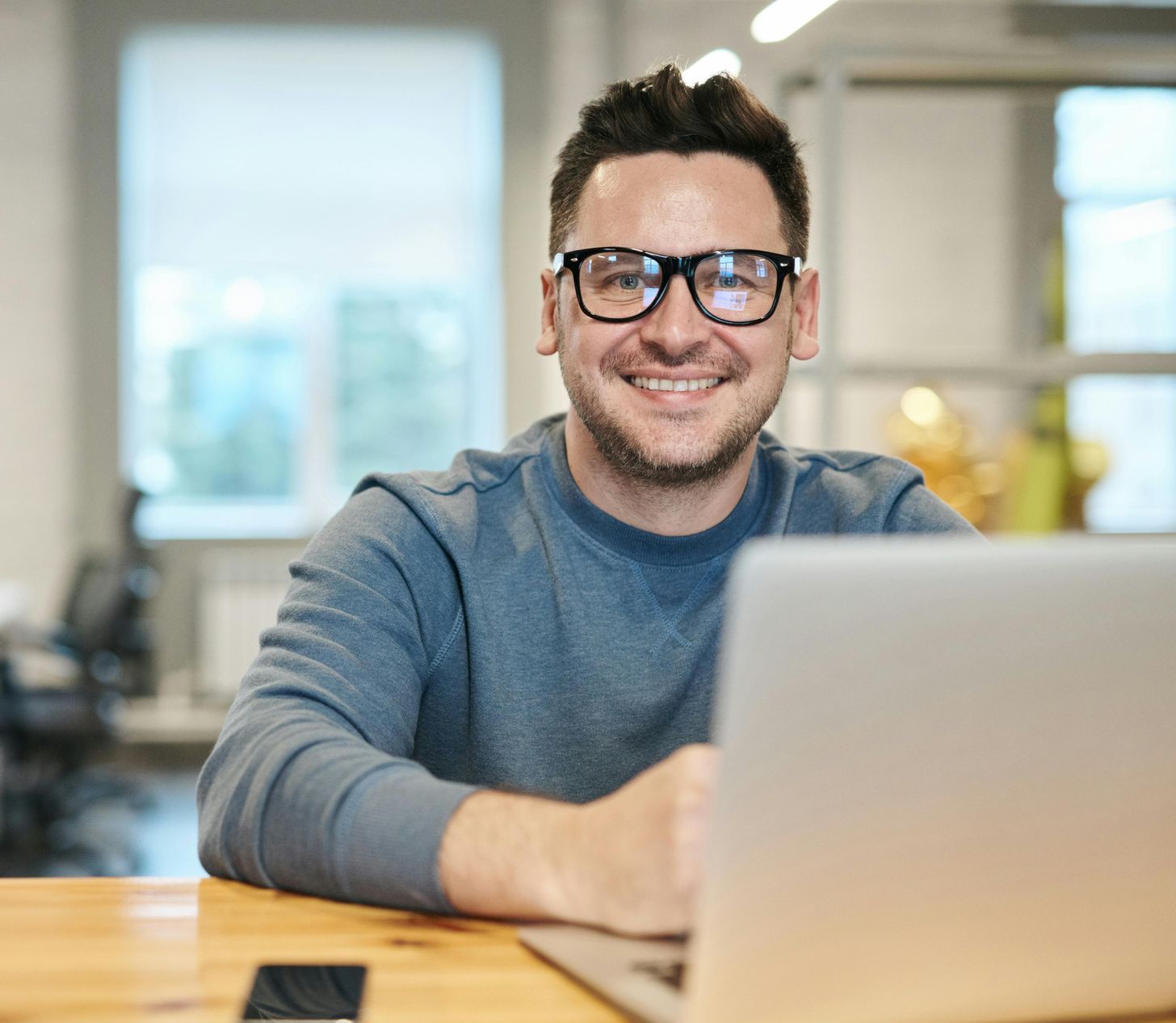 A man wearing glasses is sitting at a table using a laptop computer.