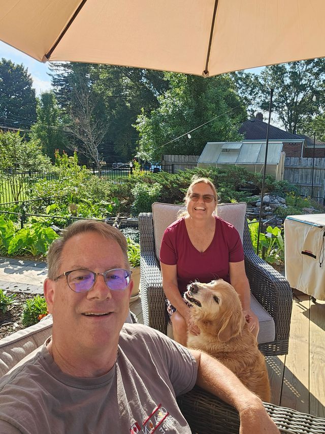 A man and a woman are sitting under an umbrella with a dog.