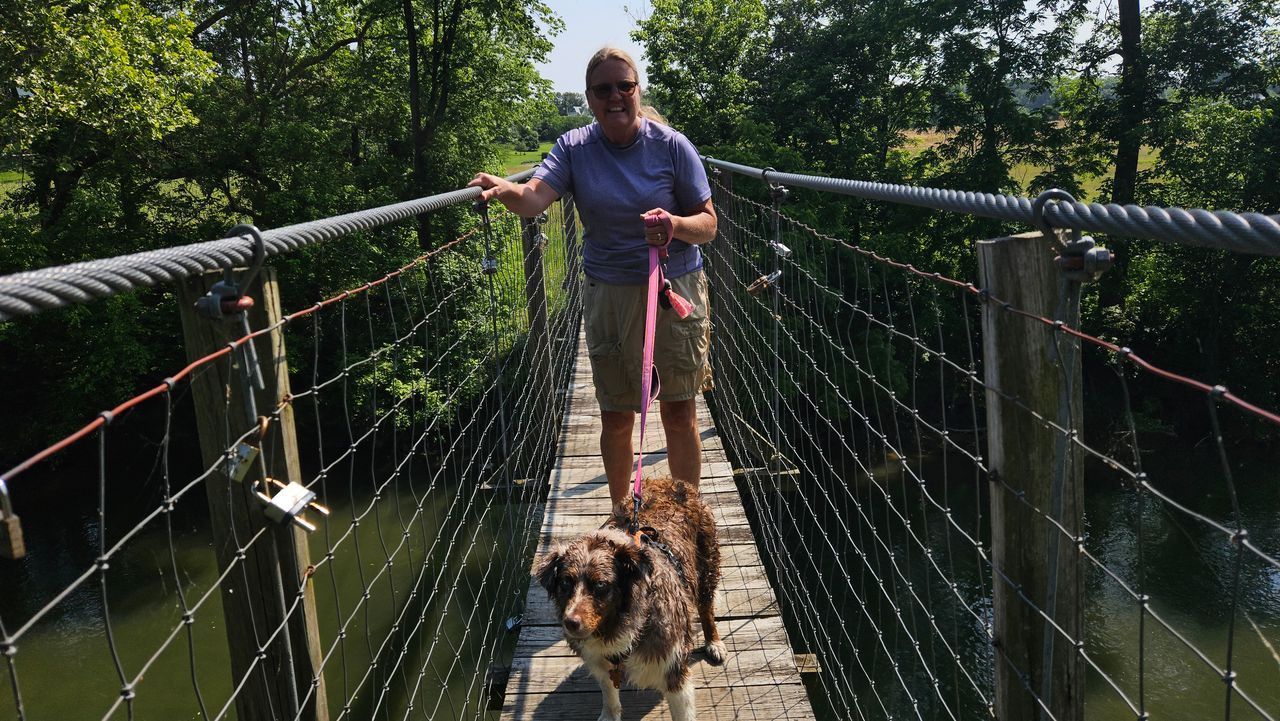 A man is walking a dog on a rope bridge over a river.
