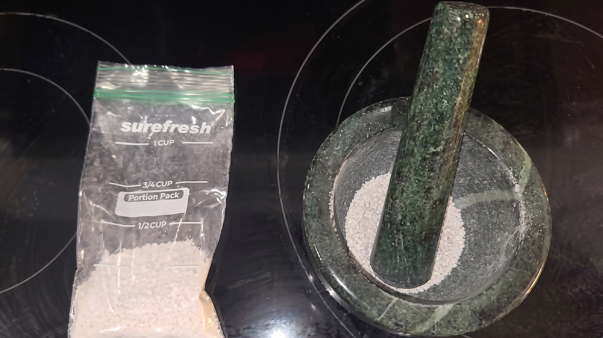 A bag of white powder beside a mortar and pestle on a dark countertop.