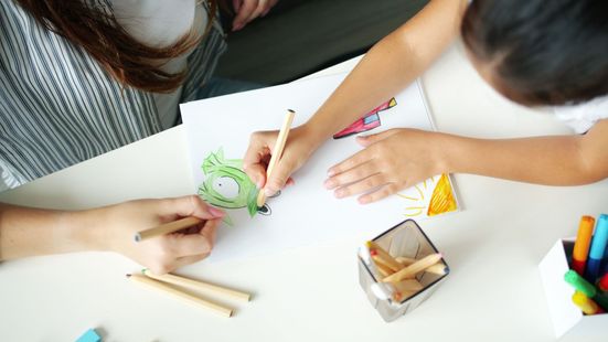 Hands and children drawing on white paper with colored pencils at a table