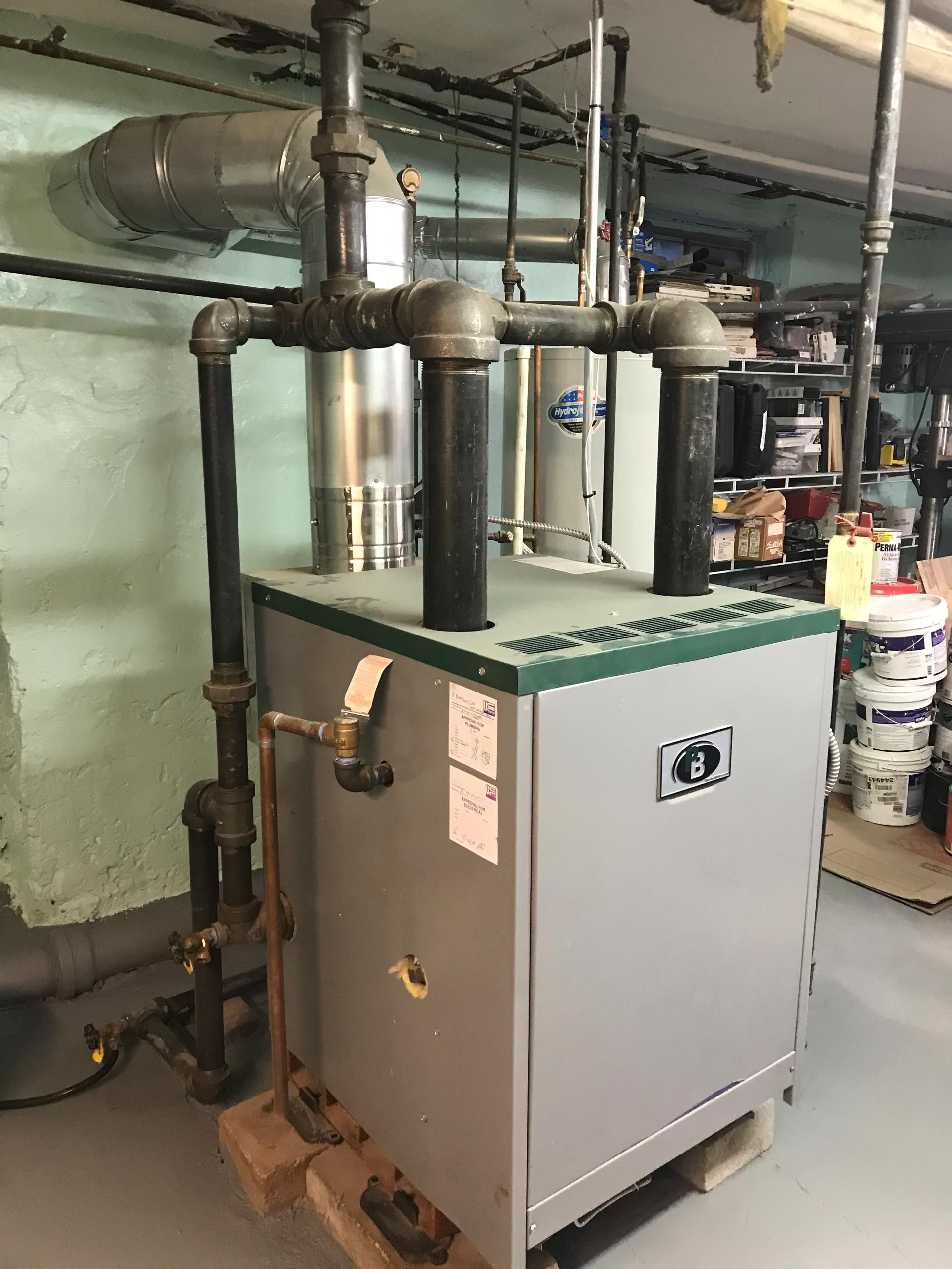 A boiler is sitting in a basement next to pipes.