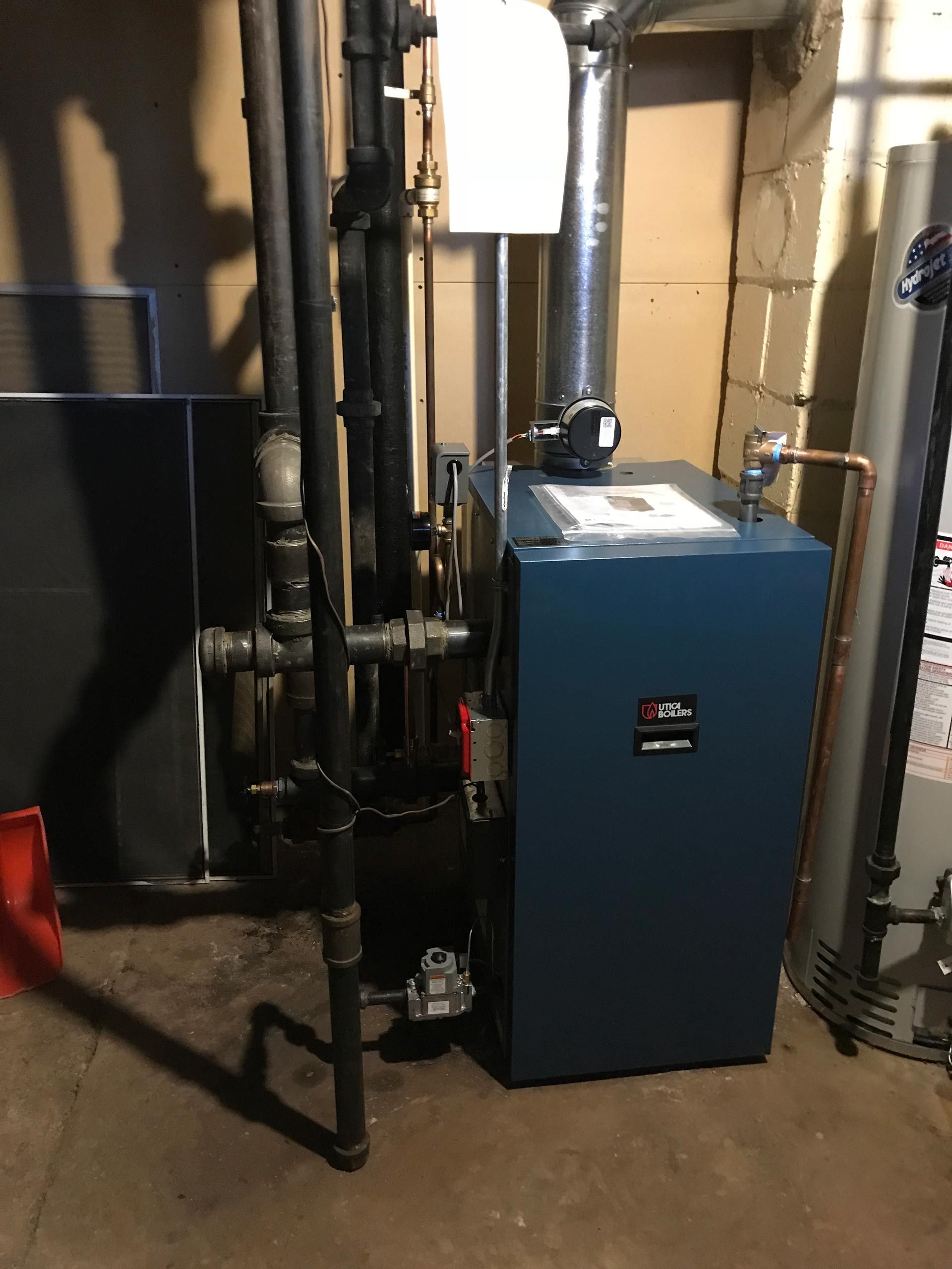 A blue boiler is sitting in a basement next to pipes.