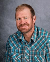 A man with a beard is wearing a blue plaid shirt.