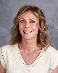 A woman wearing a white sweater and a necklace is smiling for the camera.