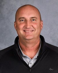 A bald man wearing a black jacket and a white shirt is smiling for the camera.