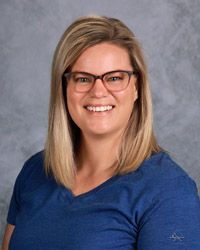 A woman wearing glasses and a blue shirt is smiling for the camera.