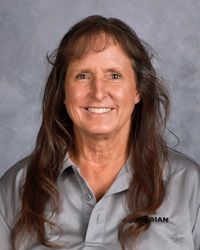 A woman with long brown hair is wearing a grey shirt and smiling for the camera.
