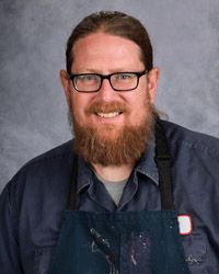 A man with a beard and glasses is wearing an apron.