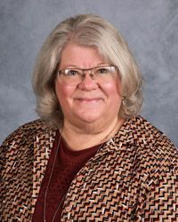 A woman wearing glasses and a jacket is smiling for the camera.