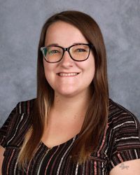 A woman wearing glasses and a striped shirt is smiling for a picture.