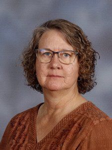 A woman wearing glasses and a brown shirt is posing for a picture.