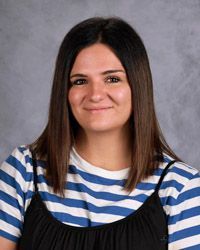 A woman in a blue and white stripe shirt with black overalls is smiling for the camera.