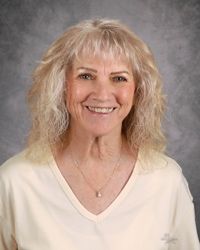Portrait of a smiling woman with curly blonde hair against a gray studio backdrop