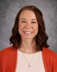 Smiling woman with shoulder-length brown hair wearing an orange cardigan against a gray backdrop