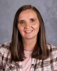 A woman in a light pink and black plaid shirt is smiling for a picture.