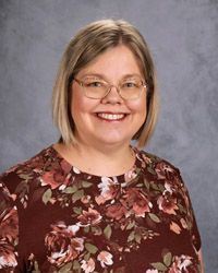 A woman wearing glasses and a maroon flower shirt is smiling for the camera.